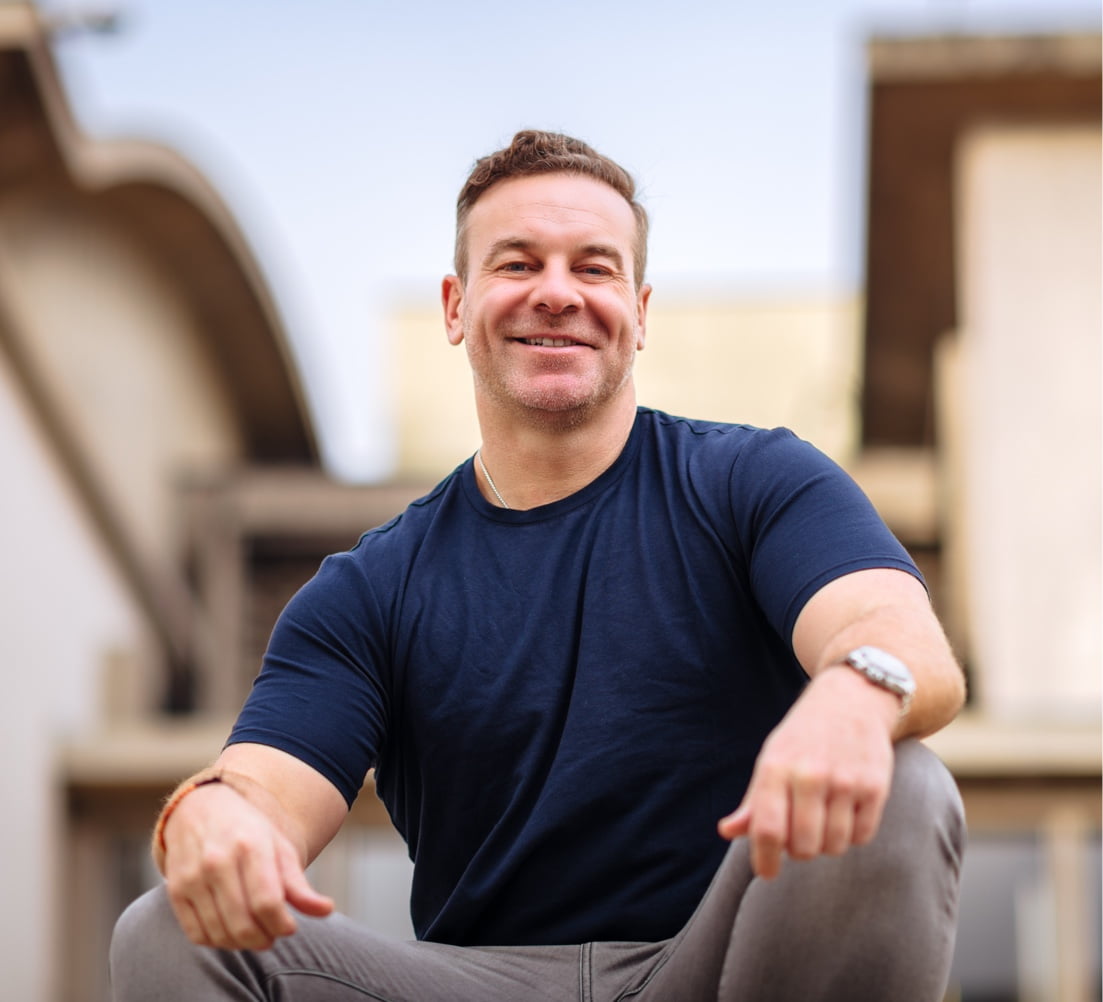 Portrait of a man outdoors with a natural landscape in the background, looking over his shoulder with a smile.