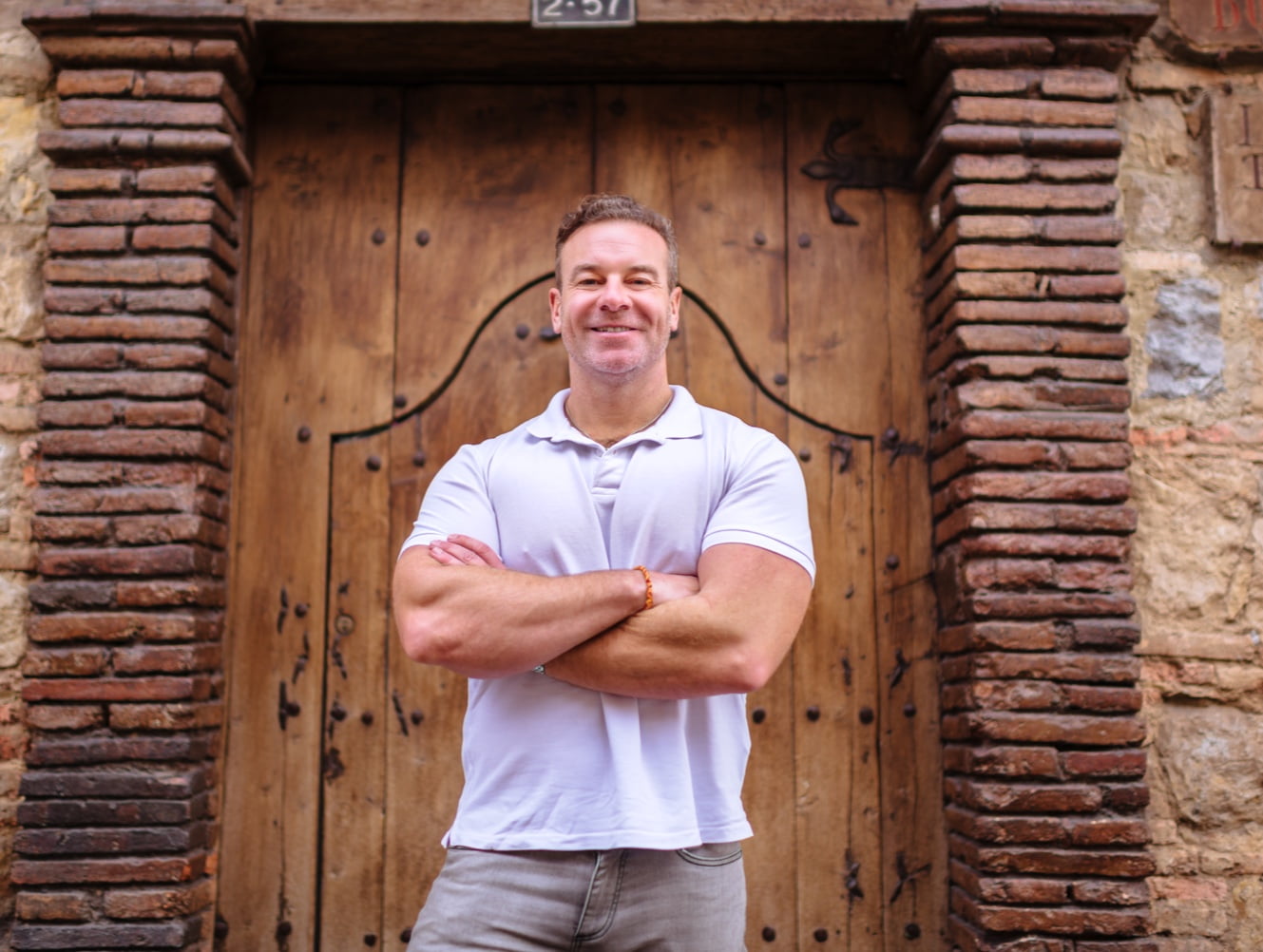 This image shows the man in a navy blue t-shirt and jeans, smiling and looking away from the camera in an urban street setting.