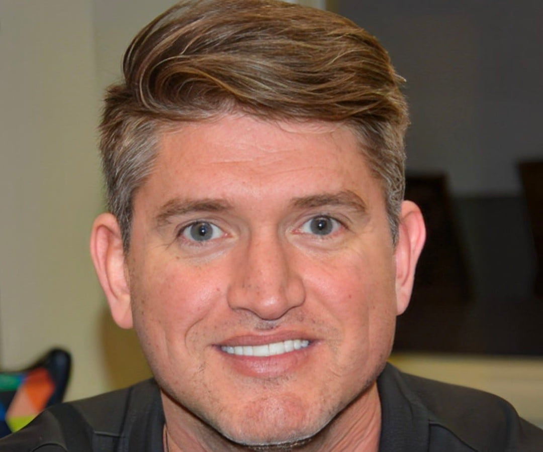 Portrait of a man smiling at the camera, with a tropical background suggesting a vacation or an exotic location.